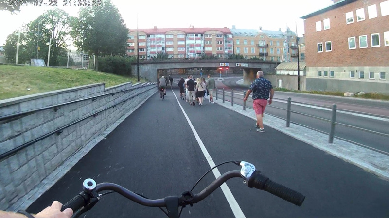 Skärmdump från en actionkamera, där bloggägaren cyklar mot en järnvägsbro i Karlstad. Till höger syns en grupp människor och rakt fram en cyklist.