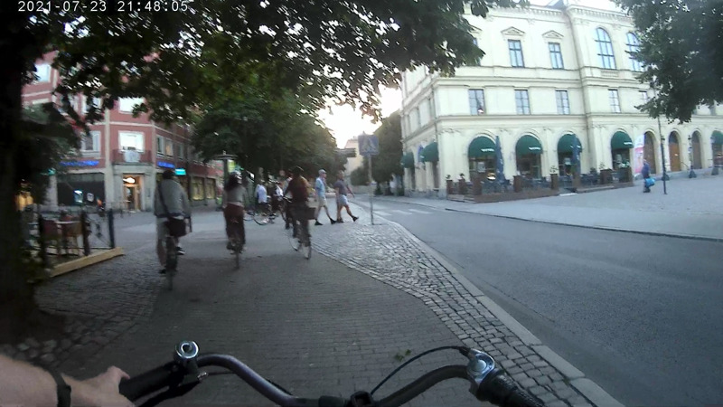 Skärmdump från en actionkamera, där bloggägaren cyklar bakom 3 cyklister som väntar på att ett gäng fotgängare ska gå förbi dom.